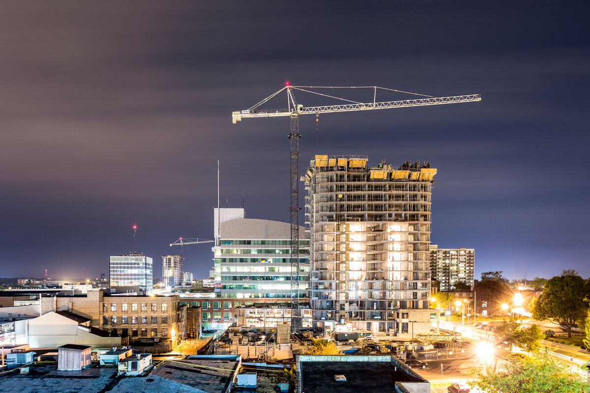 A downtown building under construction with a crane lit-up at night.