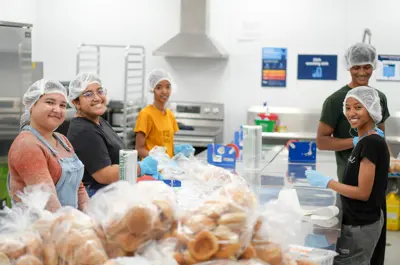 A group of young workers is smiling as they prepare food in a commercial kitchen.