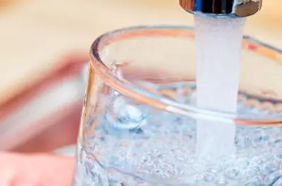 A glass being filled with clean drinking water from a sink faucet